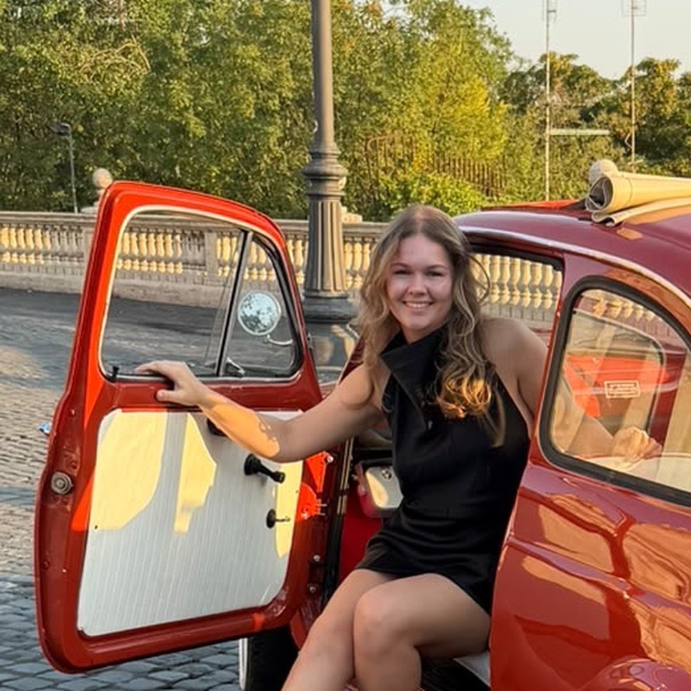 Daphne Merel, lachend, in het open portier van een rode oldtimer.